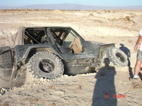 1996 Ford Bronco - A Jeep Wrangler is stuck in the dirt, with its large tires digging into the terrain.