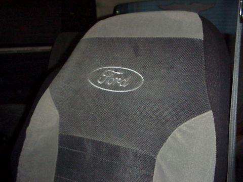 1989 Ford Bronco - Close-up of a two-tone gray and black cloth seat cover fitted over a truck seat back, with an embroidered white Ford oval logo centered on…