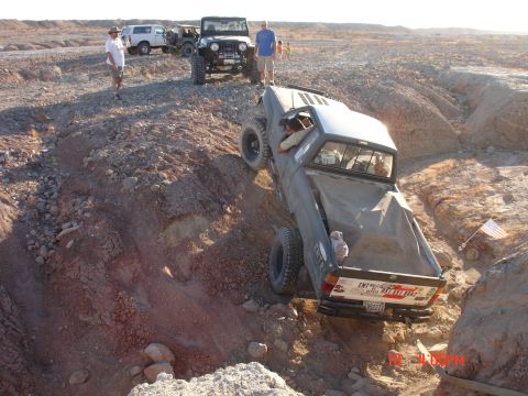 1996 Ford Bronco - Several off-road vehicles navigate a challenging desert terrain with a pickup truck descending a steep incline.