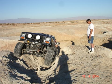 1996 Ford Bronco - An off-road SUV navigates a steep dirt incline in a desert landscape, with a person observing from the side.