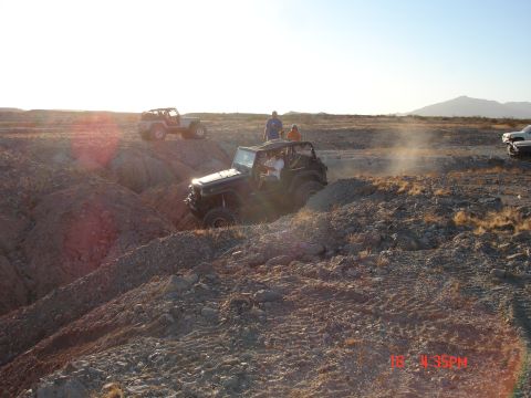 1996 Ford Bronco - Multiple Jeeps tackle a challenging off-road course, kicking up dust in the desert landscape.