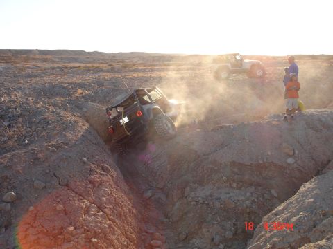 1996 Ford Bronco - Jeeps navigating challenging terrain in a dusty desert environment at sunset.