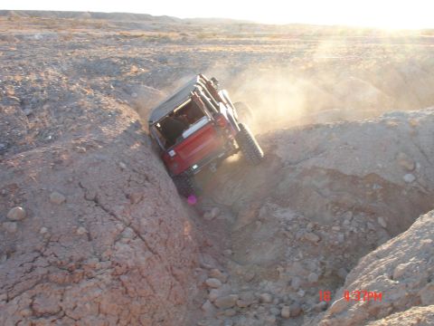 1996 Ford Bronco - A red Jeep Wrangler navigates a challenging off-road trail in a dusty, arid landscape.