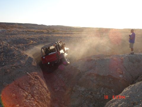 1996 Ford Bronco - A red Jeep Wrangler navigates a steep dirt ravine, with a person watching from the rim.