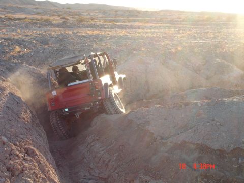1996 Ford Bronco - A red off-road vehicle navigates a challenging dirt path in a sun-drenched desert landscape.
