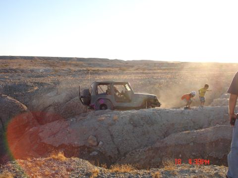1996 Ford Bronco - Off-road Jeep Wrangler navigating difficult terrain in a dusty, arid environment.