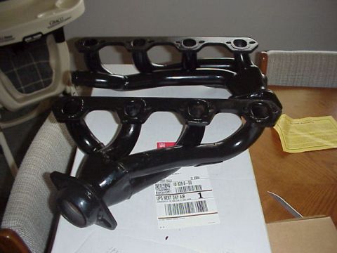 1989 Ford Bronco - A pair of new black-painted shorty exhaust headers with bare machined flange faces, resting on the shipping box and UPS Next Day Air label…