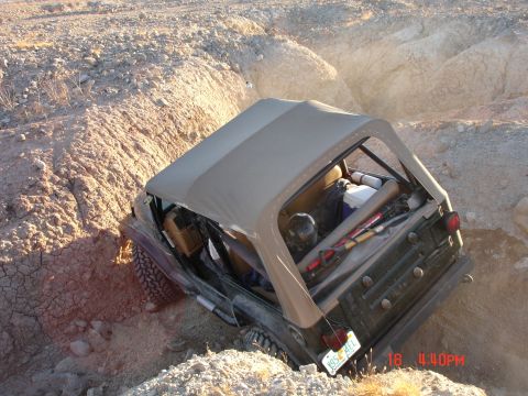 1996 Ford Bronco - A Jeep Wrangler is stuck in a deep ditch off-road, with its tires digging into the dirt.