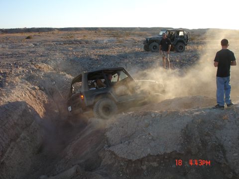 1996 Ford Bronco - Two Jeeps tackle a challenging off-road course, kicking up dust as one navigates a steep drop.