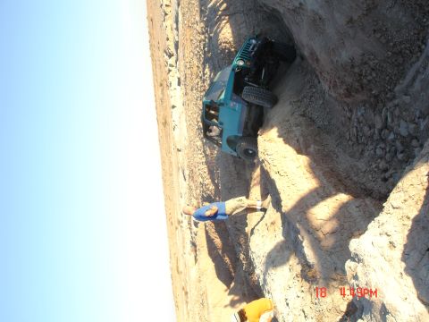 1996 Ford Bronco - A teal Jeep Wrangler is stuck in a deep ditch, with a person observing the situation.