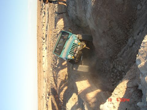 1996 Ford Bronco - A teal Jeep CJ-7 navigates a steep dirt embankment in a desert landscape.