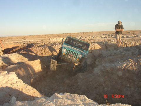 1996 Ford Bronco - A teal Jeep Wrangler navigates a challenging off-road obstacle in a desert environment.
