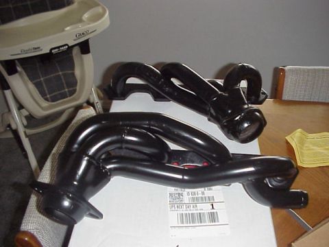 1989 Ford Bronco - A matched pair of new black-painted tubular exhaust headers sitting on the shipping box they arrived in, with a UPS Next Day Air label visi…