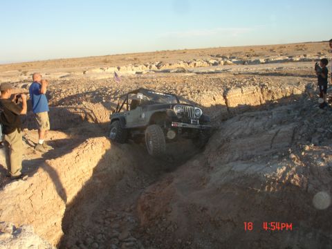 1996 Ford Bronco - A modified Jeep Wrangler tackles a challenging off-road obstacle in a dry, rocky terrain.