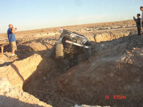 1996 Ford Bronco - A Jeep Wrangler attempts to traverse a challenging off-road trench in a desert landscape.
