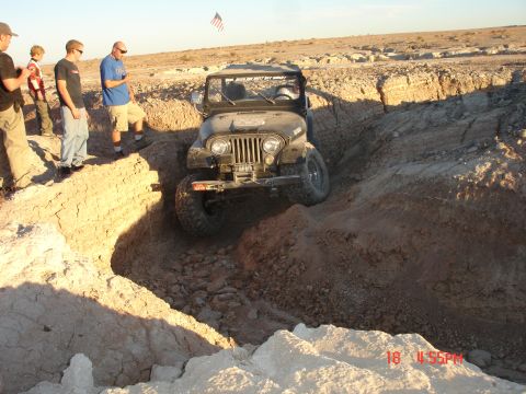 1996 Ford Bronco - A Jeep Wrangler maneuvers through a deep dirt trench in an off-road landscape.