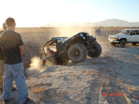 1996 Ford Bronco - Off-road Jeep with roll cage stuck in sand, white SUV in background.