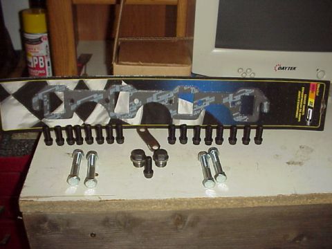 1989 Ford Bronco - A set of exhaust manifold gaskets and assorted bolts are laid out on a workbench.