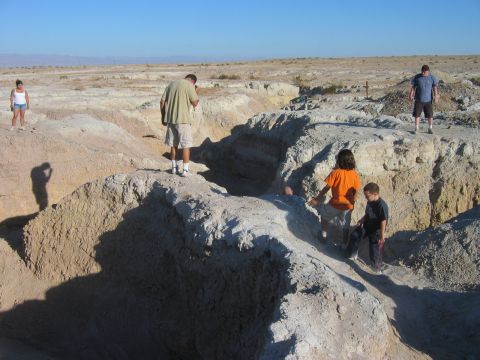 1985 Ford Bronco - Several individuals explore a , arid terrain with deep erosion channels under a bright, cloudless sky.