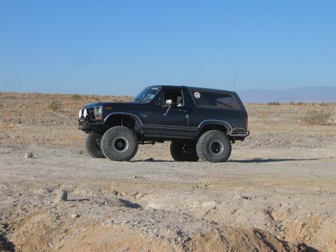 1985 Ford Bronco - Modified Ford Bronco with off-road tires sits in a dry, desert environment under a clear blue sky.