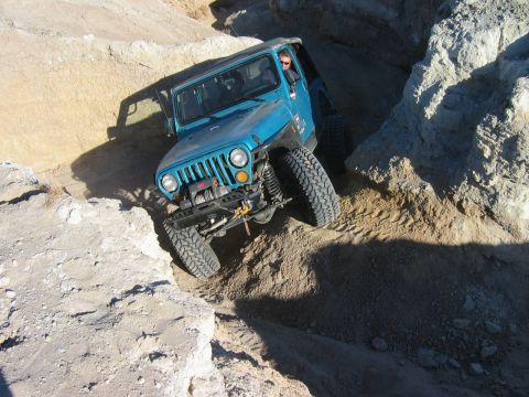 1985 Ford Bronco - A blue Jeep Wrangler tackles a challenging rocky incline, demonstrating its off-road capabilities.