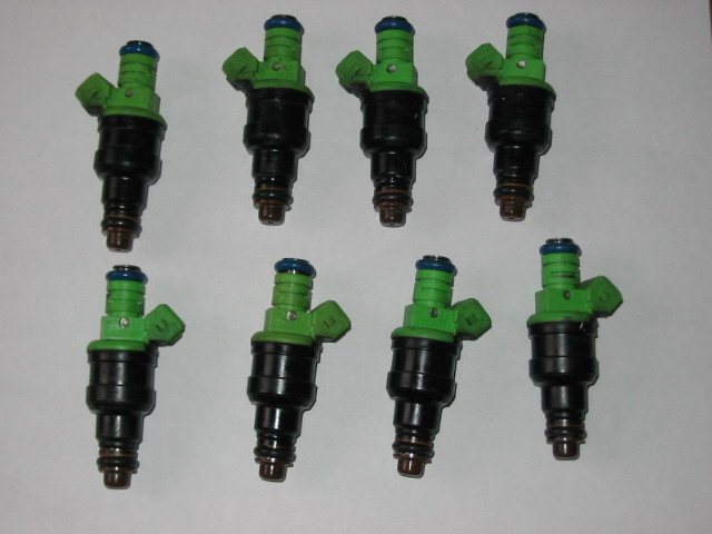 Eight black and green fuel injectors arranged in two rows on a white background