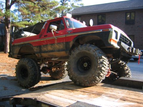1979 Ford Bronco - Modified red and black Ford Bronco with large off-road tires is loaded onto a trailer.