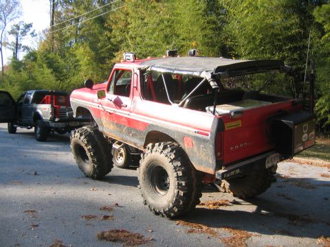 1979 Ford Bronco - Modified 1979 Ford Bronco, lifted with oversized tires and a removable soft top, sits beside a pickup truck on a paved surface.