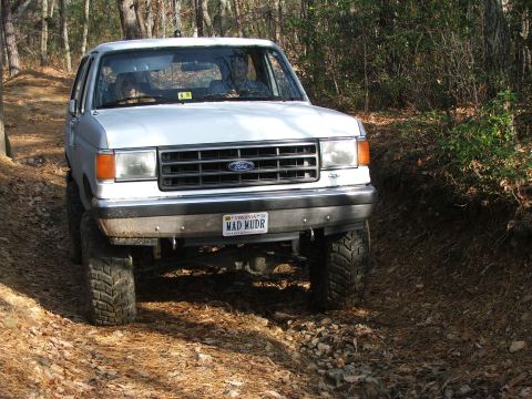 1996 Ford Bronco - White Ford Bronco with custom license plate driving off-road.