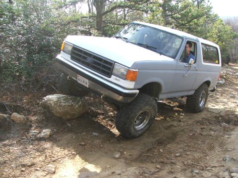 1996 Ford Bronco - A gray Ford Bronco navigates a rocky off-road trail, its tires gripping the uneven terrain.