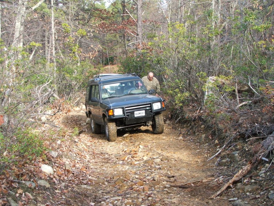 Dark blue SUV on a rocky dirt road in a wooded area
