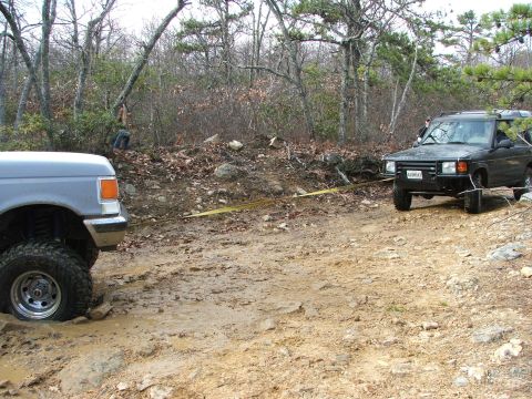 1996 Ford Bronco - Two off-road vehicles are engaged in a recovery operation on a muddy, wooded trail.