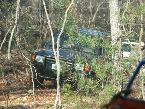 1996 Ford Bronco - A black SUV navigates a wooded trail, with another vehicle visible in the background.