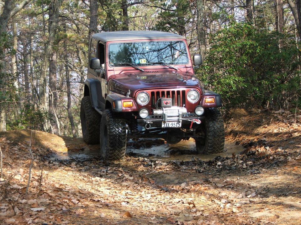 Red Jeep Wrangler driving through mud on a wooded trail