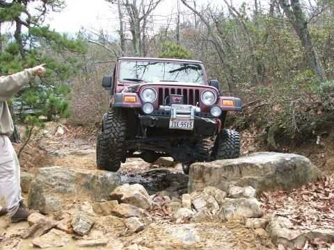 1996 Ford Bronco - A red Jeep Wrangler tackles a challenging rocky obstacle on an off-road trail.