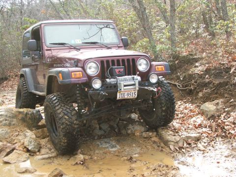 1996 Ford Bronco - Jeep Wrangler TJ Rubicon navigating a challenging off-road course with large rocks and mud.