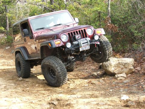1996 Ford Bronco - This modified Jeep Wrangler Rubicon is navigating a rocky trail with one wheel elevated.