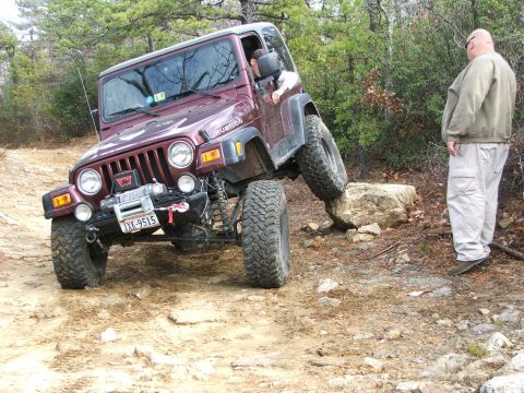 1996 Ford Bronco - A maroon Jeep Wrangler Rubicon navigates a challenging rocky trail with one wheel elevated.