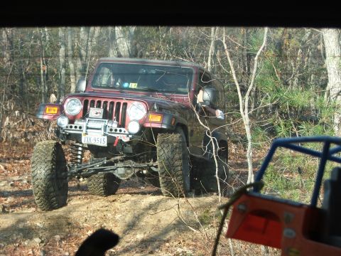 1996 Ford Bronco - A red Jeep Wrangler navigates a wooded trail, with part of another off-road vehicle visible.