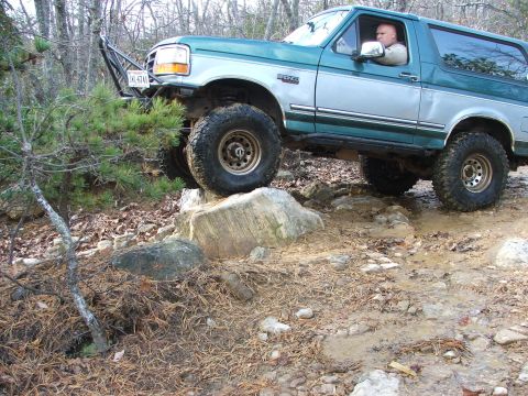1996 Ford Bronco - A 1996 Ford Bronco navigates a rocky, muddy trail in a wooded area.