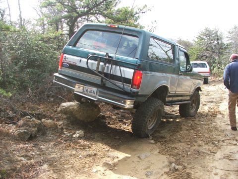 1996 Ford Bronco - A lifted 1996 Ford Bronco navigates a challenging off-road path, with one tire on a large rock.