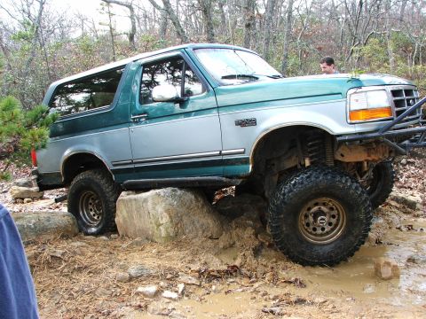 1996 Ford Bronco - A 1996 Ford Bronco navigates a challenging off-road course with mud and large rocks.