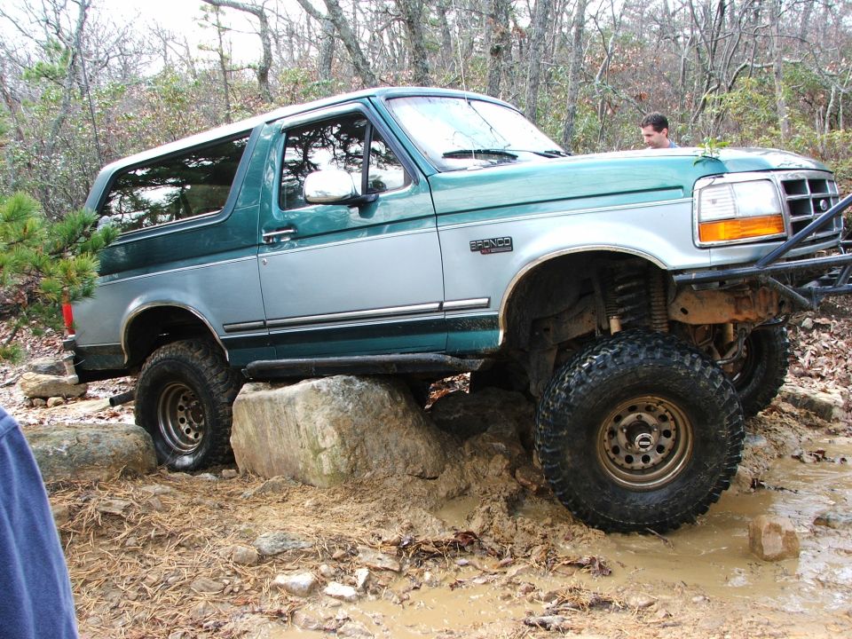 Two-tone green and silver 1996 Ford Bronco off-roading over rocks and mud