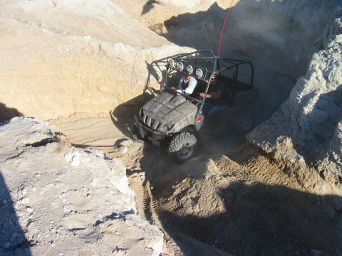 1985 Ford Bronco - This off-road vehicle is driving through a sandy terrain with rocky walls.