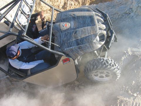 1985 Ford Bronco - Two people navigate a dusty off-road trail in a camouflage-patterned vehicle.