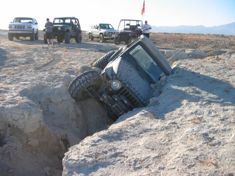 1985 Ford Bronco - A Jeep is stuck in a deep ditch off-road, with other vehicles and people observing the situation.