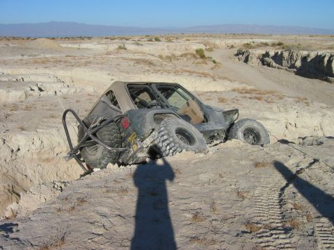 1985 Ford Bronco - Off-road buggy is stuck in a deep sandy ditch in a desert landscape.