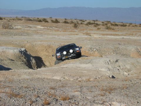 1985 Ford Bronco - A Jeep Cherokee XJ navigates a challenging off-road obstacle in a dry, desert environment.