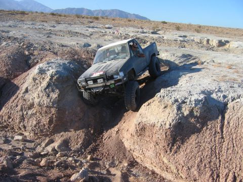 1985 Ford Bronco - A modified pickup truck navigates a challenging off-road course in a desert landscape.