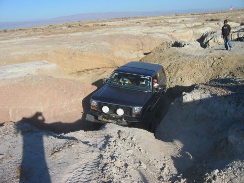 1985 Ford Bronco - Jeep Cherokee XJ tackles a challenging off-road trail in a desert landscape.